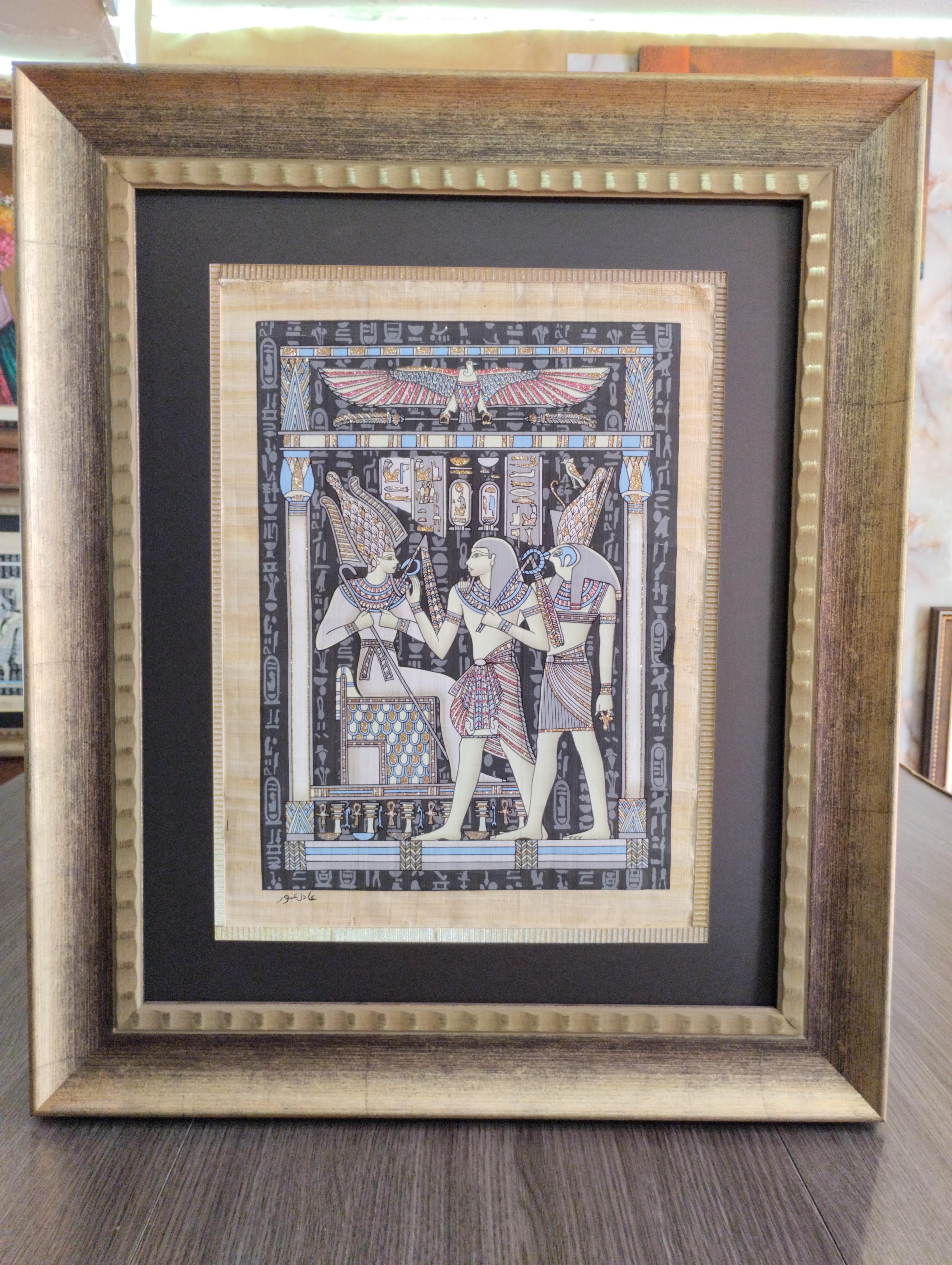 Papiro Triada Sagrada bajo Alas de Luz. Figuras egipcias de perfil junto a jeroglificos y simbolos sagrados, con detalles luminiscentes, bajo un ave alada, en marco dorado envejecido.