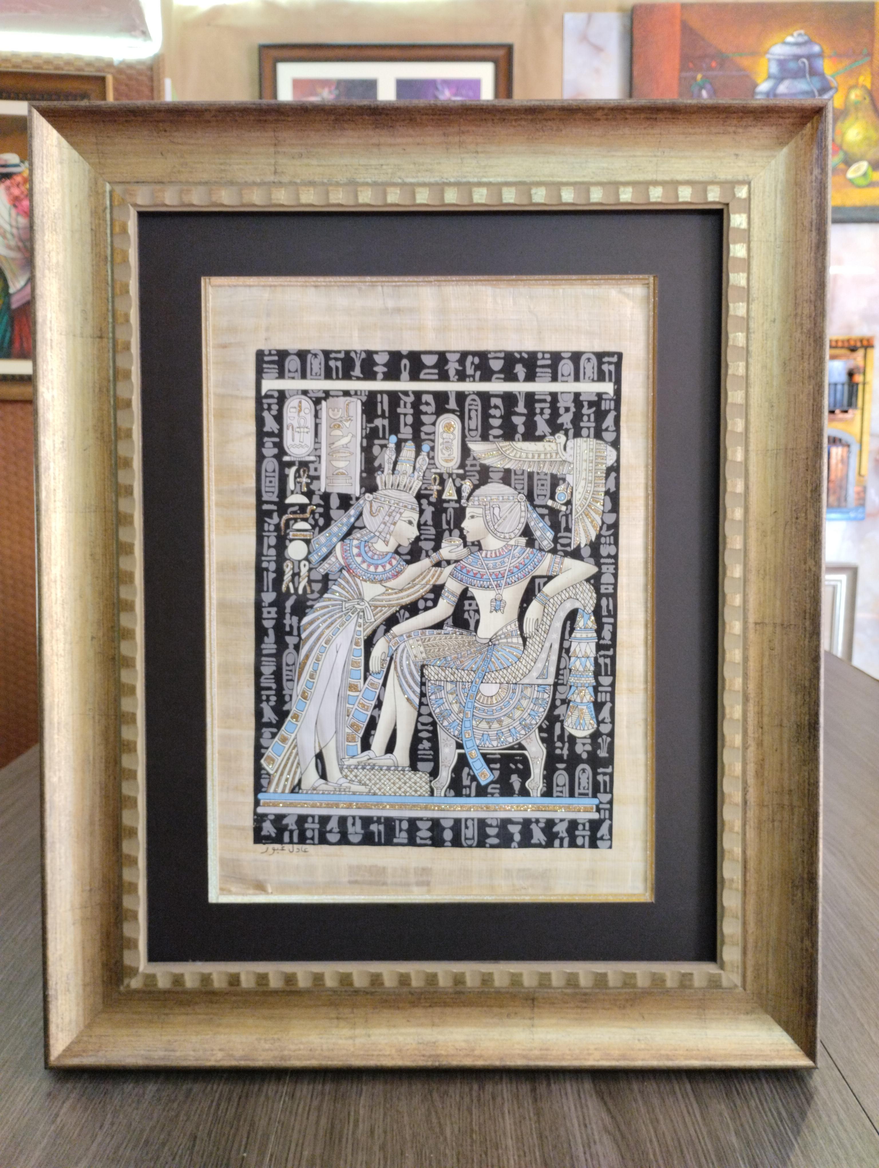 Papiro Encuentro Sagrado en Luz Eterna. Escena egipcia con dos figuras en gesto intimo rodeadas de jeroglificos, con detalles luminiscentes y marco dorado ancho de acabado envejecido.