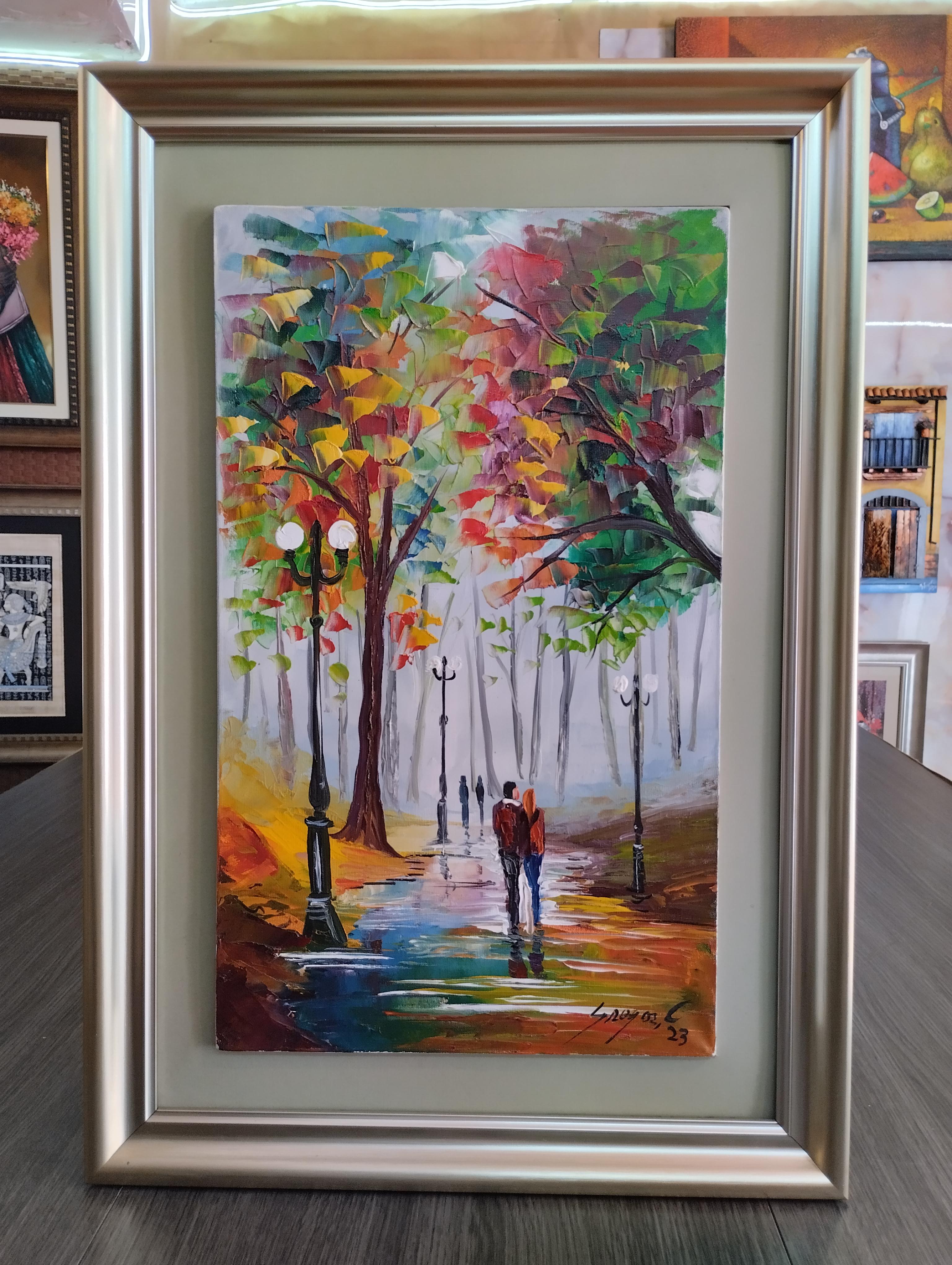 Pareja caminando. Pareja camina bajo arboles de colores vibrantes en un parque lluvioso, reflejos en el suelo y faroles encendidos, enmarcado con marco plateado elegante.
