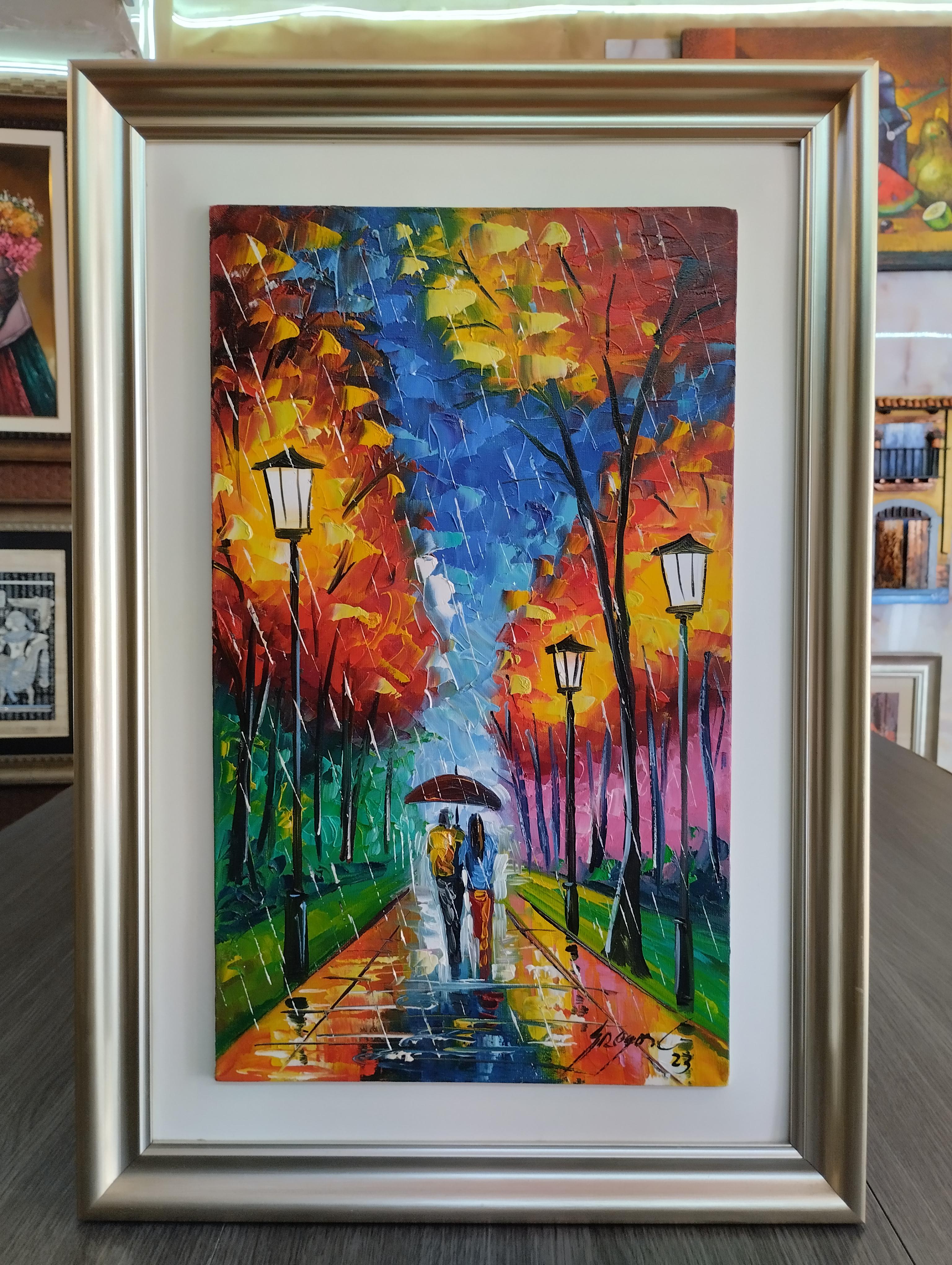 Bajo la lluvia encendida. Pareja camina bajo la lluvia con paraguas por un sendero iluminado, rodeado de arboles de colores intensos y faroles reflejados en el suelo mojado.