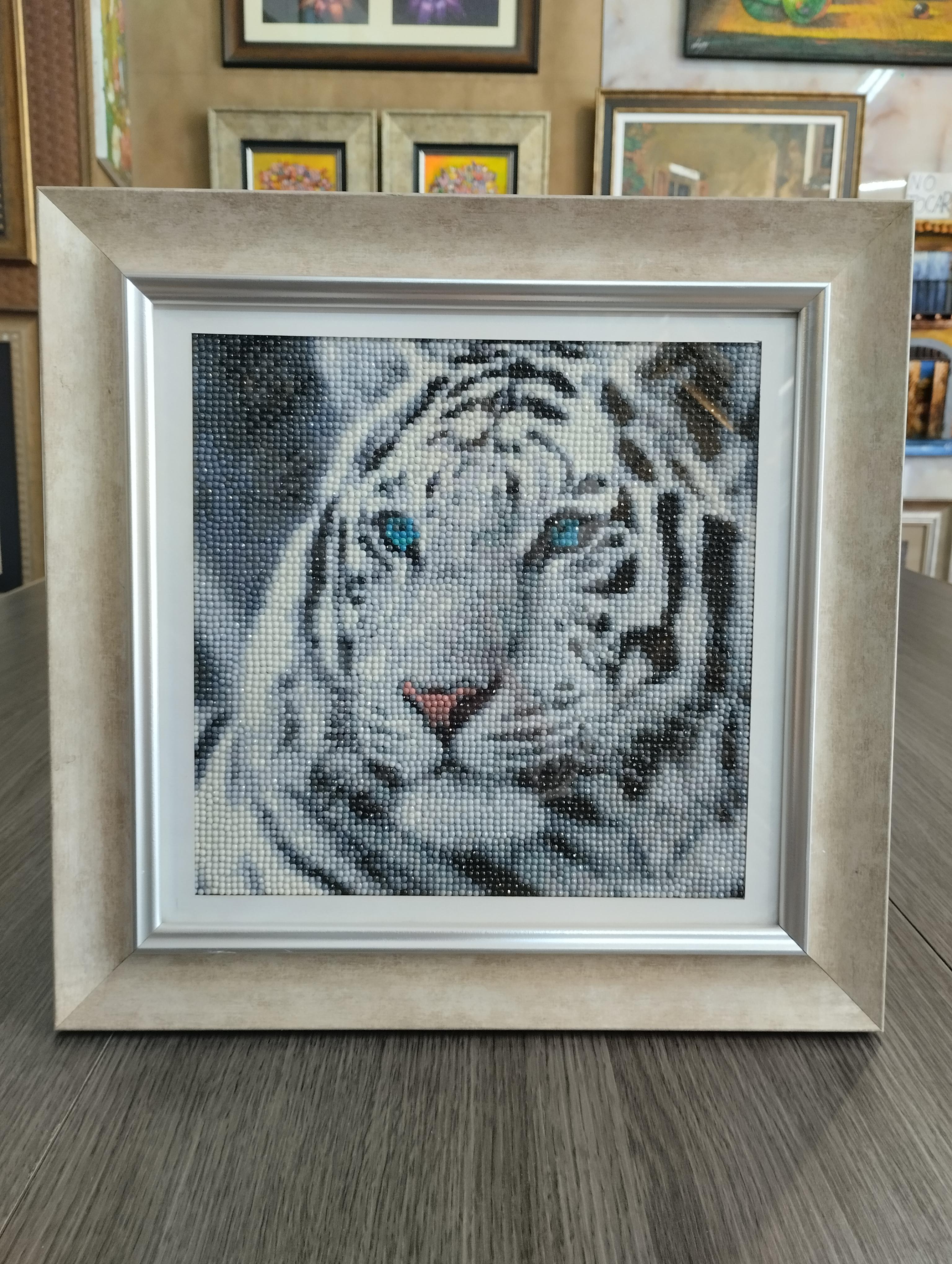 Tigre blanco. Retrato frontal de tigre blanco con ojos azules y nariz rosada, formado por pequenos puntos brillantes; marco claro ancho con acabado suave.